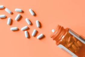 White pills spilling out of prescription bottle onto orange surface